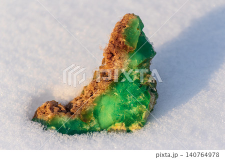 Lush green Kazakhstani chrysoprase sample, an uncut jewel, vibrantly rests on pure white winter snow, showcasing earth's raw, stunning elegance Lush green Kazakhstani chrysoprase sample, an uncut jewel, vibrantly rests on pure white winter snow, showcasing earth's raw, stunning elegance 140764978