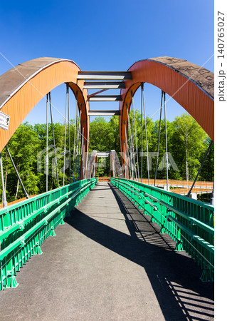 Modern orange pedestrian bridge with vibrant green railings stands as a pathway over a busy highway, framed against a clear blue summer sky providing a perfect urban infrastructure view 140765027