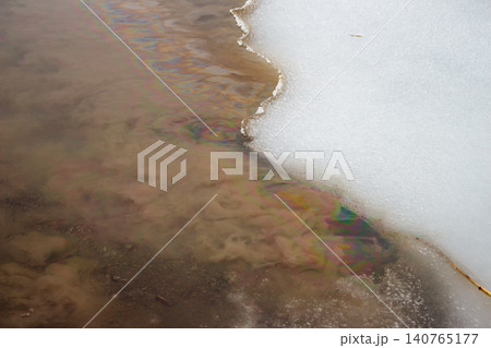 Vibrant, toxic oil slick paints a dirty river, merging with melting snow. A harsh environmental warning of pollution and ecological damage Vibrant, toxic oil slick paints a dirty river, merging with melting snow. A harsh environmental warning of pollution and ecological damage 140765177