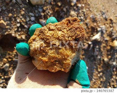 Gloved hand proudly holding a raw quartz secretion, a fascinating geological find from a sunny quarry expedition. Discovery moment Gloved hand proudly holding a raw quartz secretion, a fascinating geological find from a sunny quarry expedition. Discovery moment 140765387