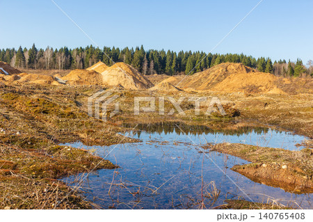 Spring thaw unveils a dormant sand quarry: shimmering puddles reflect the clear sky amidst golden earth mounds. A rugged, natural landscape emerging Spring thaw unveils a dormant sand quarry: shimmering puddles reflect the clear sky amidst golden earth mounds. A rugged, natural landscape emerging 140765408