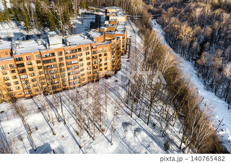 Aerial view of a sprawling apartment building nestled beside a snow-covered forest during winter, capturing the stark beauty of a cold landscape Aerial view of a sprawling apartment building nestled beside a snow-covered forest during winter, capturing the stark beauty of a cold landscape 140765482