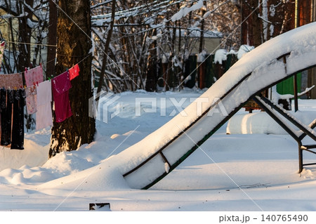Deserted children's slide blanketed by fresh, pristine snow, glowing under soft winter sunshine. A silent, frosty scene, evoking peaceful cold Deserted children's slide blanketed by fresh, pristine snow, glowing under soft winter sunshine. A silent, frosty scene, evoking peaceful cold 140765490