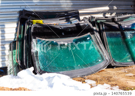 Stacked pile of discarded cracked automotive windshields leaning against a metallic industrial workshop wall awaiting recycling or disposal in an outdoor area Stacked pile of discarded cracked automotive windshields leaning against a metallic industrial workshop wall awaiting recycling or disposal in an outdoor area 140765539