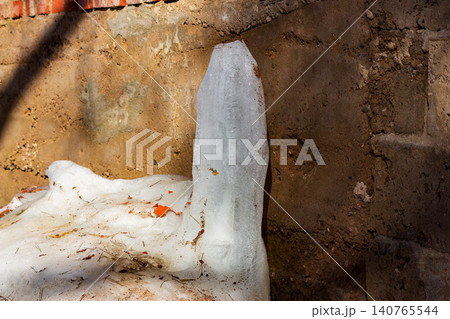 Melting icicle standing against a rustic textured concrete garage wall during early spring thaw, close-up view of thawing ice structures on a sunny day Melting icicle standing against a rustic textured concrete garage wall during early spring thaw, close-up view of thawing ice structures on a sunny day 140765544