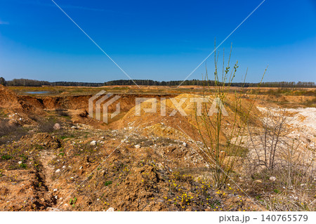 Small open-pit limestone quarry for gravel extraction with reddish soil piles and a stagnant water pool under a clear blue sky on a bright spring day Small open-pit limestone quarry for gravel extraction with reddish soil piles and a stagnant water pool under a clear blue sky on a bright spring day 140765579