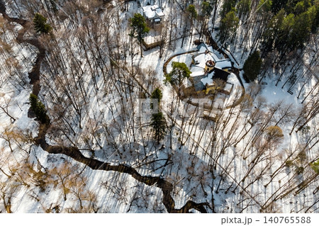 Charming snow-kissed estate house from above, nestled within a serene wintry forest. A dark, winding stream threads through the tranquil, white landscape. Turliki manor, Obninsk, Russia Charming snow-kissed estate house from above, nestled within a serene wintry forest. A dark, winding stream threads through the tranquil, white landscape. Turliki manor, Obninsk, Russia 140765588