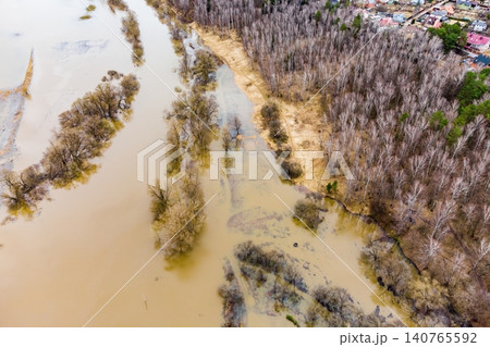 Drone shot captures a vast, muddy spring flood engulfing riverside trees and lowlands. A dramatic natural high-water scene Drone shot captures a vast, muddy spring flood engulfing riverside trees and lowlands. A dramatic natural high-water scene 140765592