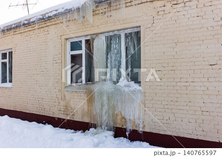 A brick building's window encased in a dramatic cascade of thick ice and sharp icicles. Winter's freezing power clearly visible, transforming the urban landscape into a frigid art piece A brick building's window encased in a dramatic cascade of thick ice and sharp icicles. Winter's freezing power clearly visible, transforming the urban landscape into a frigid art piece 140765597