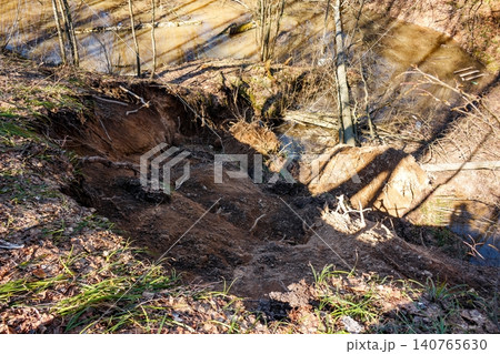 Vivid springtime landslide showcases raw, sandy slope erosion, with exposed roots tumbling into a narrow ravine. A testament to nature's relentless reshaping power Vivid springtime landslide showcases raw, sandy slope erosion, with exposed roots tumbling into a narrow ravine. A testament to nature's relentless reshaping power 140765630