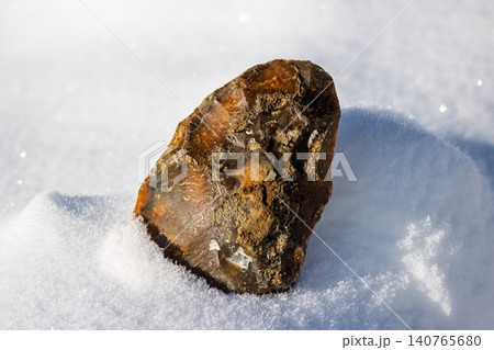 Hand-knapped primitive flint tool replica rests on sparkling pristine snow under bright sun. Ancient Paleolithic craftsmanship artifact 140765680