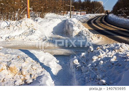 Deeply cleared pedestrian path between massive dirty snow berms and a winding winter road under bright sunlight Deeply cleared pedestrian path between massive dirty snow berms and a winding winter road under bright sunlight 140765695