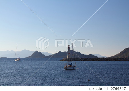 Seascape at sunshine. Lighthouse and sailings on the coast. Seaside town of Turgutreis and spectacular sunshine Seascape at sunshine. Lighthouse and sailings on the coast. Seaside town of Turgutreis and spectacular sunshine 140766247