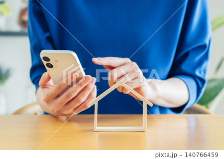 住宅模型とスマホを持つ若い女性の手元 住宅模型とスマホを持つ若い女性の手元 140766459