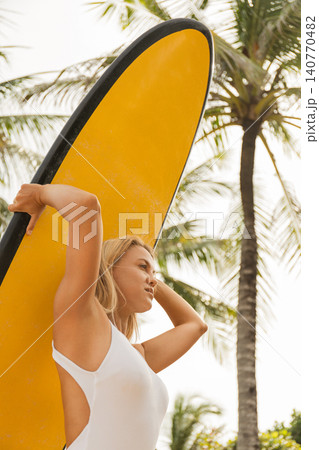 Young woman holds surfboard while enjoying sunny beach vibes Young woman holds surfboard while enjoying sunny beach vibes 140770482