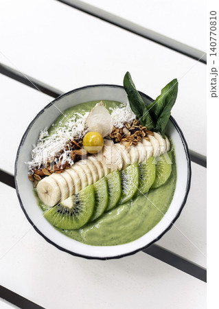 mixed fruit breakfast buddha bowl with banana, kiwi, coconut and granola on outdoor cafe white table 140770810