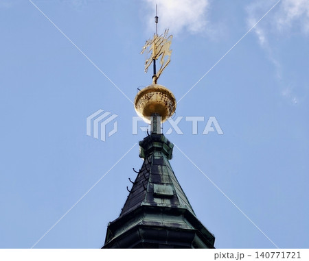 Gilded weather vane atop tower. Ancient structure crowned with metallic symbol and decorative features Gilded weather vane atop tower. Ancient structure crowned with metallic symbol and decorative features 140771721