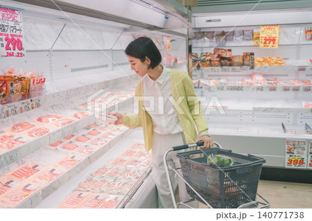 スーパーの精肉売り場でパック肉を手に取り選ぶ若い女性客 スーパーの精肉売り場でパック肉を手に取り選ぶ若い女性客 140771738