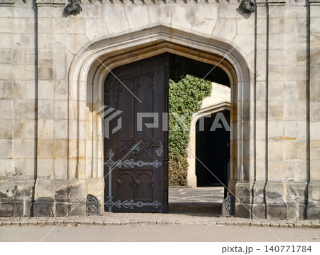 Ancient wooden gate leads to sunny courtyard area. Timeworn oak door opens onto sunny old cloister scene Ancient wooden gate leads to sunny courtyard area. Timeworn oak door opens onto sunny old cloister scene 140771784