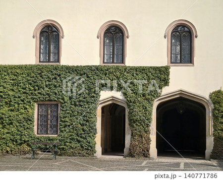 Charming historic facade with arched windows. Timeless courtyard scene featuring ivy and aged stone Charming historic facade with arched windows. Timeless courtyard scene featuring ivy and aged stone 140771786