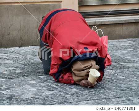Person wearing red jacket kneels with head bowed on icy sideway in front of weathered wall Person wearing red jacket kneels with head bowed on icy sideway in front of weathered wall 140771801