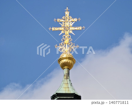 Intricately designed gilded cross finial illuminated by sunlight on sacred building rooftop Intricately designed gilded cross finial illuminated by sunlight on sacred building rooftop 140771811