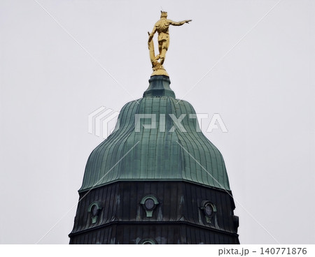 Golden monument panorama. Urban landmark featuring gilded figure and weathered architectural features Golden monument panorama. Urban landmark featuring gilded figure and weathered architectural features 140771876