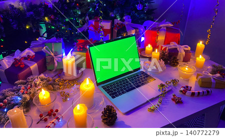 New Year computer concept. Laptop with a chroma key on the screen lies on the Christmas table. Wrapped gift boxes, burning candles, pine cones, confetti, fir branch with red berries New Year computer concept. Laptop with a chroma key on the screen lies on the Christmas table. Wrapped gift boxes, burning candles, pine cones, confetti, fir branch with red berries 140772279