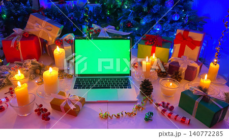 Gift boxes, burning candles, cones, confetti, a fir branch with red berries and striped caramel. Personal computer with a chroma key on the screen lies on the New Year's table. Gift boxes, burning candles, cones, confetti, a fir branch with red berries and striped caramel. Personal computer with a chroma key on the screen lies on the New Year's table. 140772285
