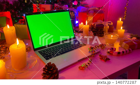 An open laptop with a chroma key on the screen lies on a white wooden table. Christmas gifts, burning candles, cones, confetti, fir branches and striped caramel. Workplace An open laptop with a chroma key on the screen lies on a white wooden table. Christmas gifts, burning candles, cones, confetti, fir branches and striped caramel. Workplace 140772287