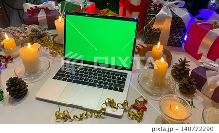 Freelancer's desktop decorated with New Year's gifts, burning candles, cones, confetti, fir branches and striped caramel. An open laptop with a chroma key Freelancer's desktop decorated with New Year's gifts, burning candles, cones, confetti, fir branches and striped caramel. An open laptop with a chroma key 140772290