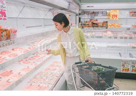 スーパーの精肉売り場でパック肉を手に取り選ぶ若い女性客 140772319
