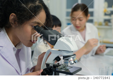 Young black woman using microscope in science laboratory with teacher in background Young black woman using microscope in science laboratory with teacher in background 140772841