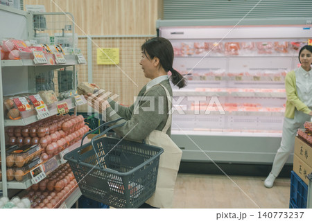 スーパーでたまごを確認する中高年女性客と背景の若い女性 スーパーでたまごを確認する中高年女性客と背景の若い女性 140773237