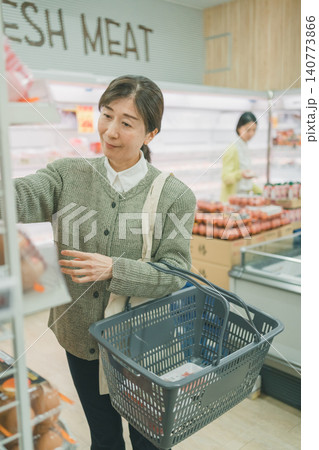 スーパーのたまご売り場で卵を選ぶ中高年女性客と背景の若い女性 スーパーのたまご売り場で卵を選ぶ中高年女性客と背景の若い女性 140773866