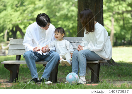公園のベンチに座ってくつろぐ若い夫婦と愛娘 公園のベンチに座ってくつろぐ若い夫婦と愛娘 140773927