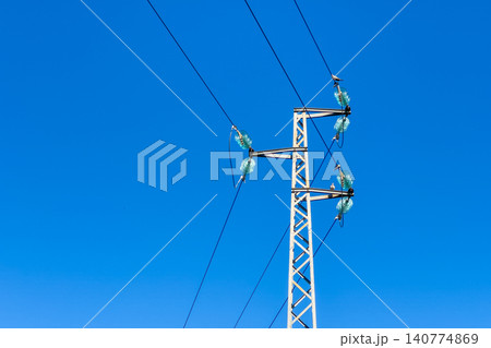 A stark white metal electricity pylon stands against a vibrant blue sky A stark white metal electricity pylon stands against a vibrant blue sky 140774869