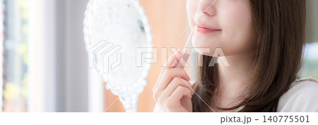 手鏡を見ながらリップを塗る女性　リップグロスや唇のケアなどのイメージクローズアップ顔無しのバナー 140775501