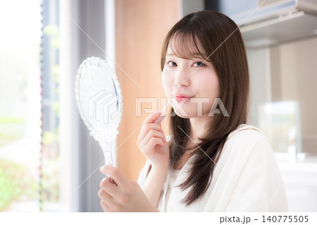 手鏡を持つリップを塗る女性のナチュラルメイクと美容ケア リップグロスや唇のケアなどのカメラ目線笑顔 手鏡を持つリップを塗る女性のナチュラルメイクと美容ケア リップグロスや唇のケアなどのカメラ目線笑顔 140775505