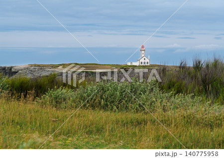 White Lighthouse on Rugged Coastal Cliffs Overlooking Grassy Seaside Landscape Under Cloudy Sky 140775958