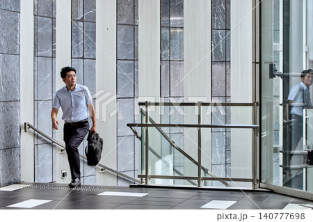 出社の為にオフィスビルで階段を登る半袖シャツを着た30代の日本人のビジネスマンの男性 出社の為にオフィスビルで階段を登る半袖シャツを着た30代の日本人のビジネスマンの男性 140777698