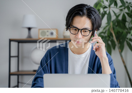 自宅でスマホで通話しながらパソコンを見る男性 自宅でスマホで通話しながらパソコンを見る男性 140778416