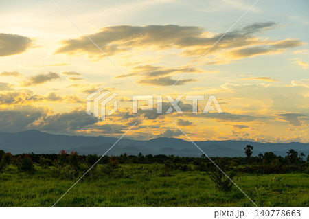Scenic landscape of green grass field and mountains under golden sunset sky. 140778663