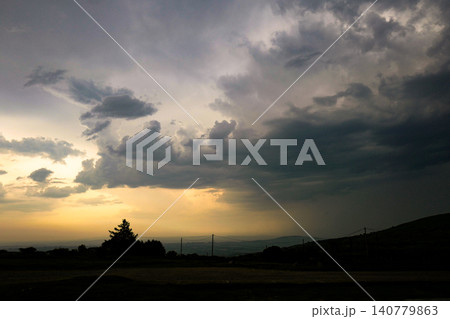 This dramatic scene depicts a stormy sunset with clouds breaking to reveal golden light. The atmosphere resembles a rare optical weather phenomenon, where sunset colours glow behind dark storm clouds This dramatic scene depicts a stormy sunset with clouds breaking to reveal golden light. The atmosphere resembles a rare optical weather phenomenon, where sunset colours glow behind dark storm clouds 140779863