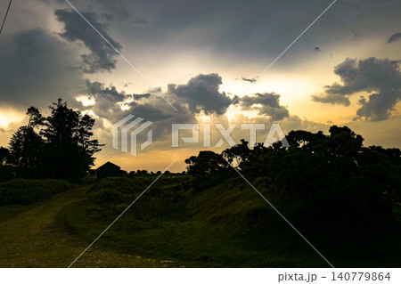 This dramatic scene depicts a stormy sunset with clouds breaking to reveal golden light.  The atmosphere resembles a rare optical weather phenomenon, where sunset colours glow behind dark storm clouds 140779864