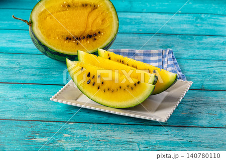 Yellow watermelon slices on white plate with blue wooden background 140780110