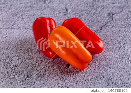Three fresh red and orange bell peppers on textured gray surface 140780163