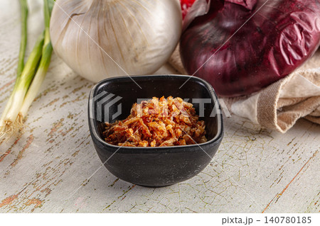 Crispy fried onions in black bowl with garlic and red onion on rustic wood Crispy fried onions in black bowl with garlic and red onion on rustic wood 140780185