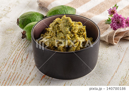 Green fruit paste in dark bowl with whole fruits and purple flowers on rustic wood 140780186