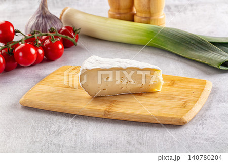 Slice of soft cheese on wooden board with cherry tomatoes garlic and leek Slice of soft cheese on wooden board with cherry tomatoes garlic and leek 140780204